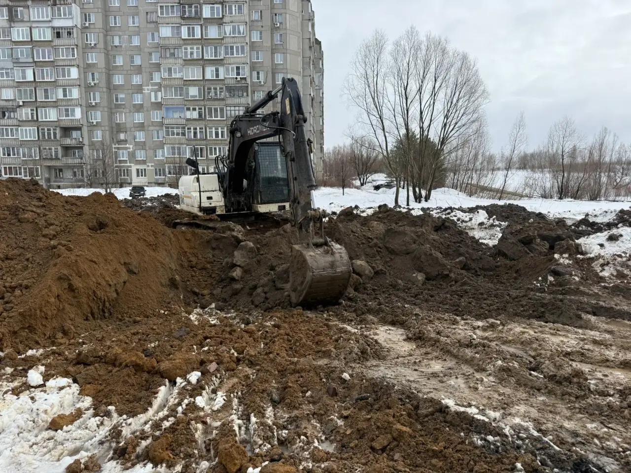 Земляные работы экскаватором на территории рядом с жилым домом